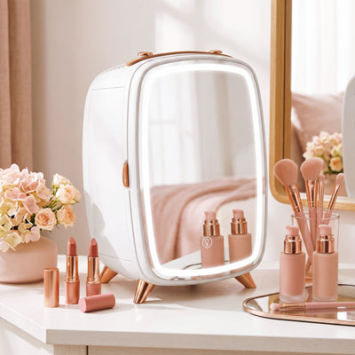 White mini fridge on a dressing table beside flowers, lipsticks and makeup brushes
