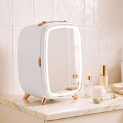 White fridge with its lit mirror closed on a marble surface beside serum and a jade roller