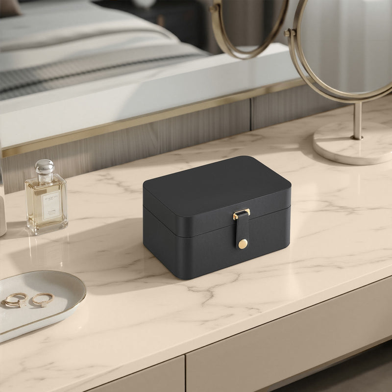 Closed slate grey travel jewellery case styled on a bedroom dresser beside a perfume bottle and mirror