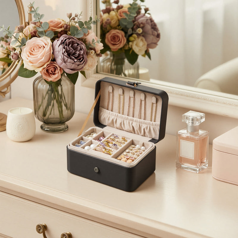 Open slate grey jewellery case on a dresser with flowers and a candle, storing rings, earrings and necklaces