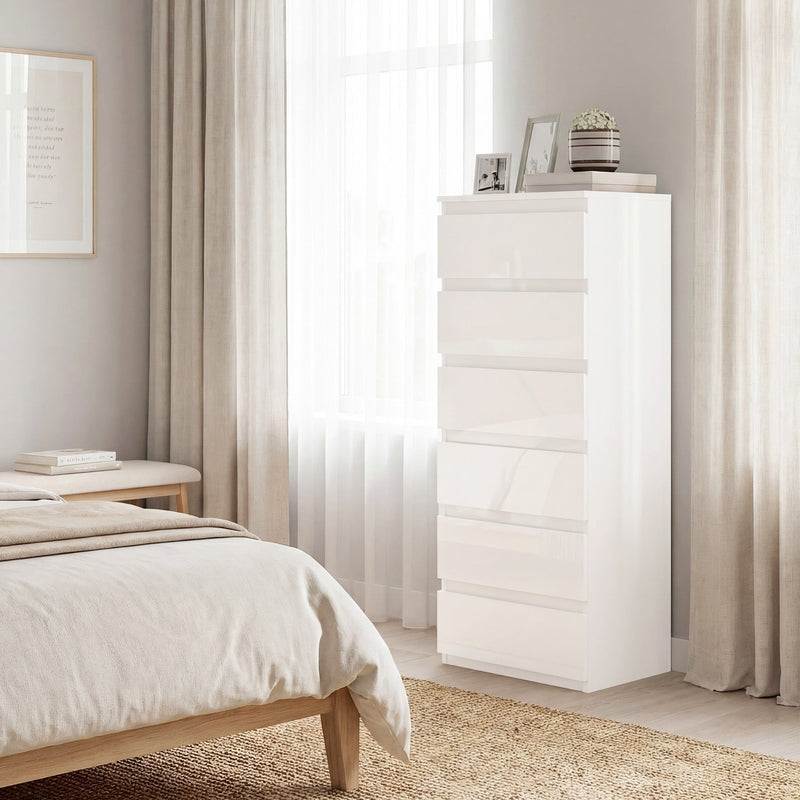 Tall white chest of drawers beside a bed near a sunlit curtained window