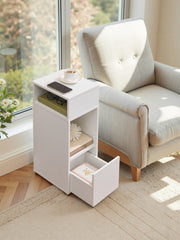 Bedside table beside an armchair by a window with the bottom drawer pulled open