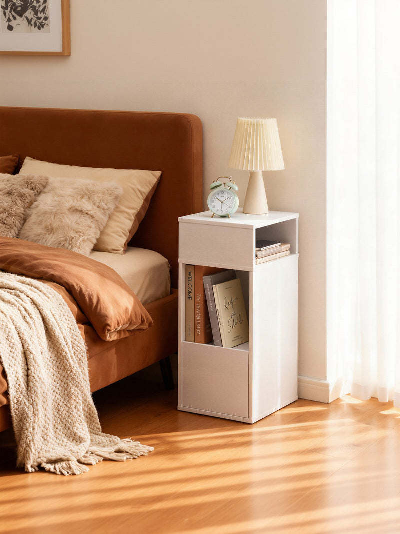 White bedside table next to a bed holding a lamp, an alarm clock and books