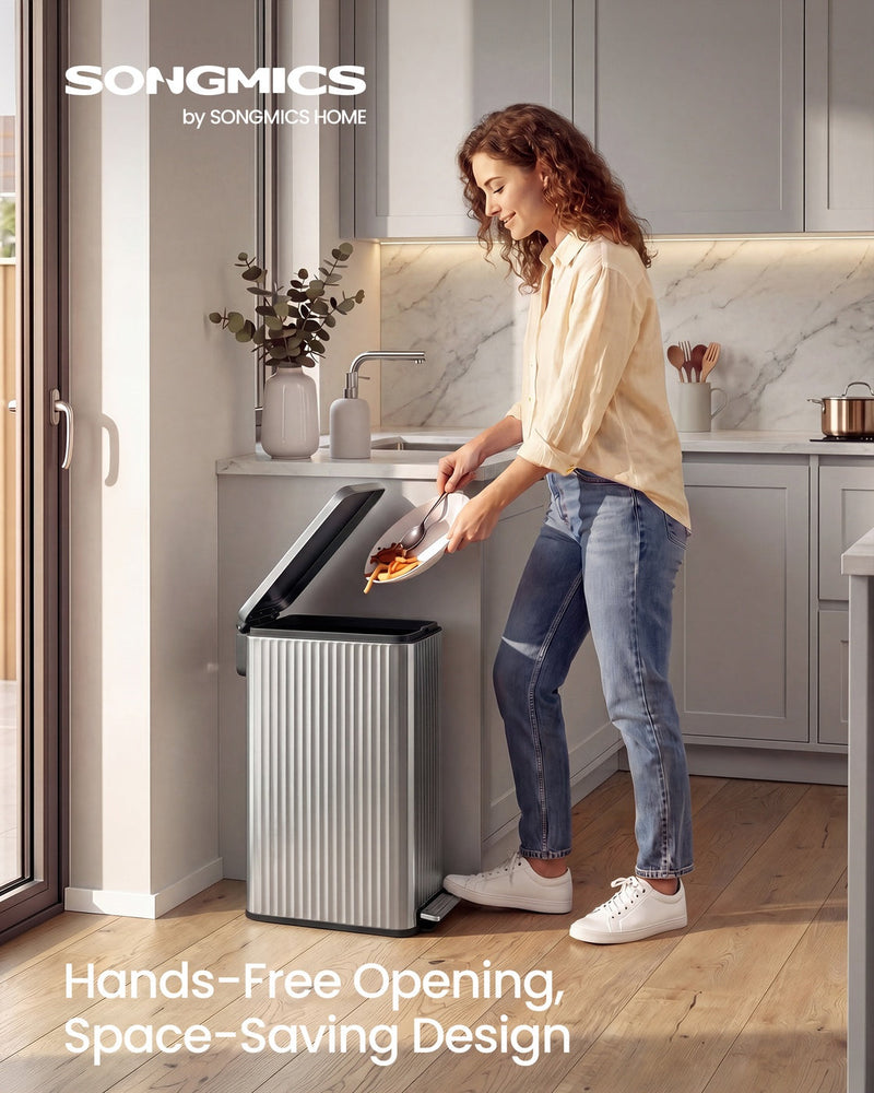 Woman in a grey kitchen scraping food waste from a pan into the open Songmics 50 L silver pedal bin standing beside the cabinets
