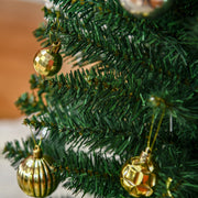 Close-up of green branch tips hung with gold baubles