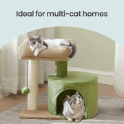 Two cats sharing the green cat tree on a rug, one on the top bed and one in the condo