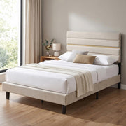 Beige upholstered bed frame with white bedding in a bedroom with a window and wooden floor