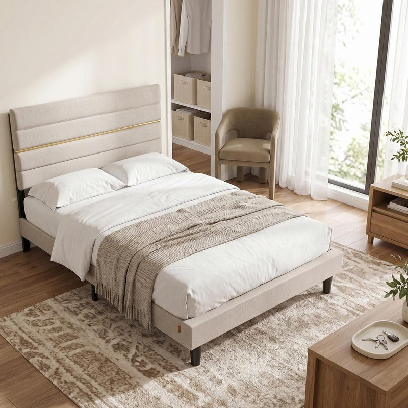 Beige bed frame with bedding in a bedroom beside a wardrobe and armchair