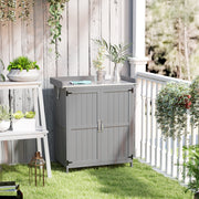Grey wooden storage shed on a lawn beside a white balcony railing with potted plants on the worktop
