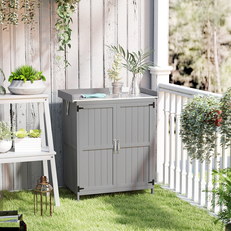 Grey wooden storage shed on a lawn beside a white balcony railing with potted plants on the worktop