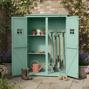 Green shed against a brick wall with potted plants on the roof and garden tools stored inside