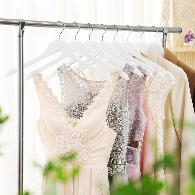 White wooden hangers on a rail holding lace dresses and a beige jacket