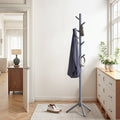 Grey solid wood coat rack standing in a bright hallway beside a chest of drawers, holding a jacket, bag and headphones