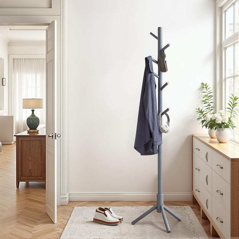 Grey solid wood coat rack standing in a bright hallway beside a chest of drawers, holding a jacket, bag and headphones