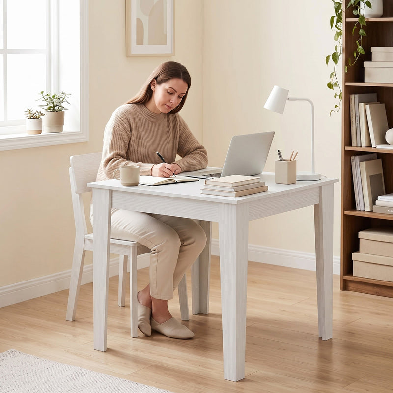 White dining table used as a home workspace with a laptop and desk lamp