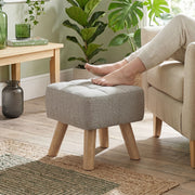 Bare feet resting on the light brown footstool beside an armchair