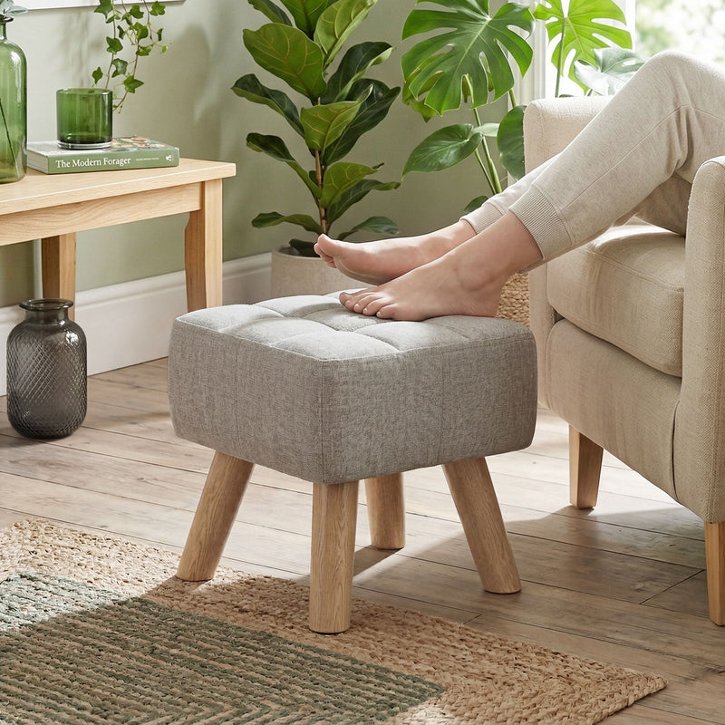 Bare feet resting on the light brown footstool beside an armchair