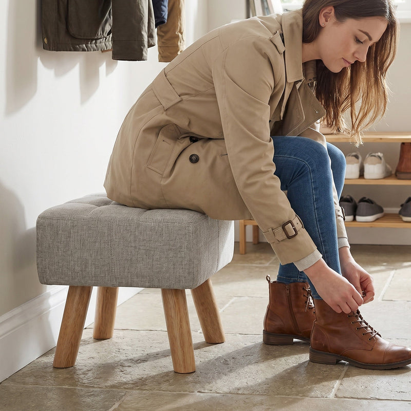 Woman sitting on the footstool while tying her boots in a hallway