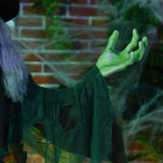 Close-up of the witch's green hand and dark green robe against a brick wall