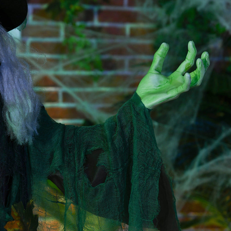 Close-up of the witch's green hand and dark green robe against a brick wall