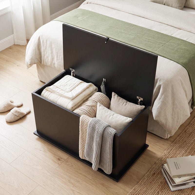 Overhead view of the black storage bench packed with folded bedding, cushions and a knitted throw