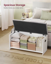 Storage bench at the foot of a bed with the lid open and folded clothes, pillows and books inside
