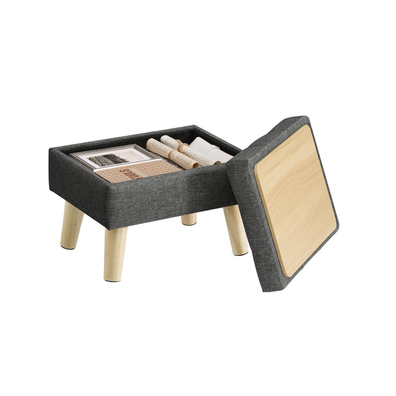 Slate grey linen-look storage ottoman with wooden legs shown with its hinged lid lifted open to reveal books stored inside the hollow compartment.