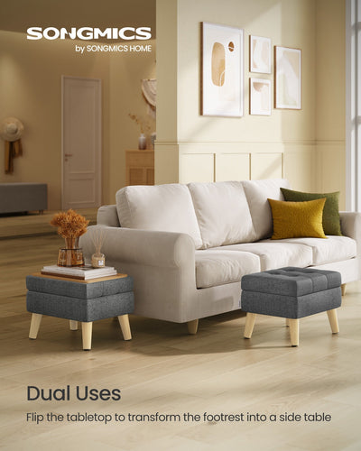 Two slate grey storage ottomans of different sizes used as flip-top side tables beside a cream sofa, one holding a diffuser and stacked books.