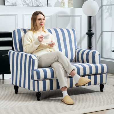 Woman holding a teacup while sitting in the striped armchair beside a globe floor lamp