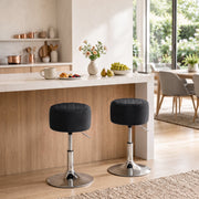 Two black swivel stools at a light wood kitchen island with a dining area in the background
