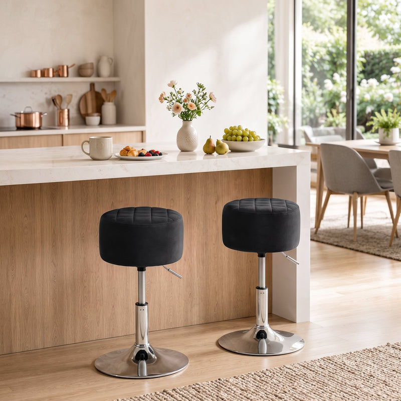 Two black swivel stools at a light wood kitchen island with a dining area in the background