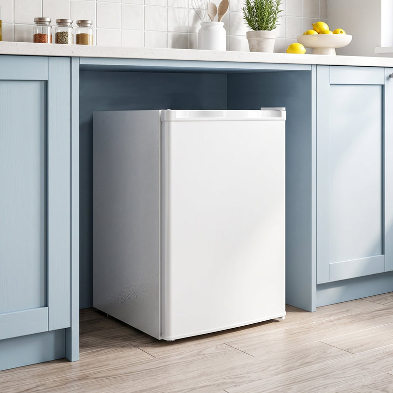 Mini freezer standing in a gap beneath a kitchen worktop with blue cabinets