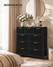 Black 9-drawer corduroy chest of drawers in a bedroom with flowers and a round mirror