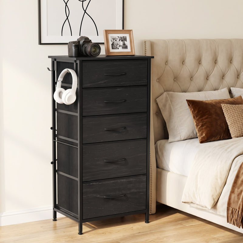 Tall chest beside a tufted bed with a camera on top and headphones on the hook, shown in black