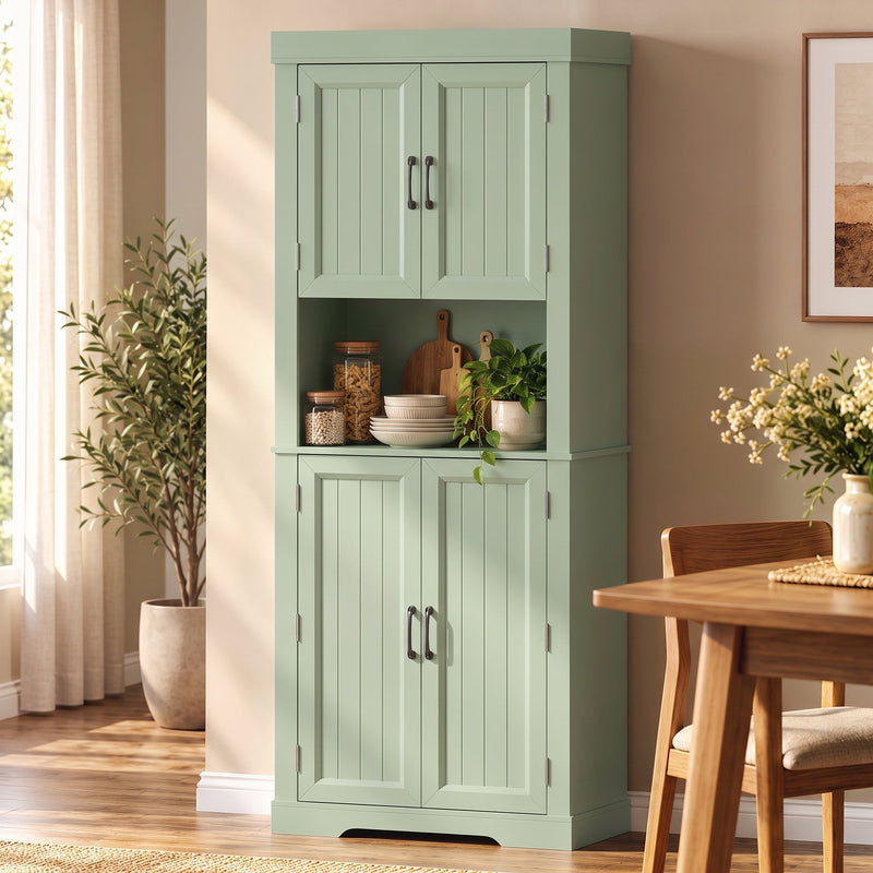 Sage green kitchen cupboard beside a dining table with crockery and a plant on the open counter