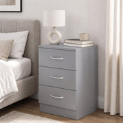 Grey bedside table beside a bed with a white lamp, mug and books on top