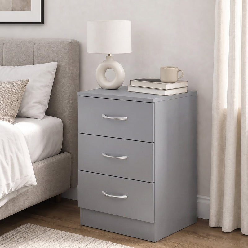 Grey bedside table beside a bed with a white lamp, mug and books on top