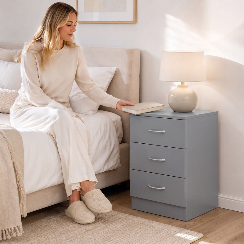 Woman sitting on a bed reaching for a book on the grey bedside table