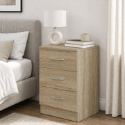 Oak bedside table beside a bed with a lamp, books and a mug on top