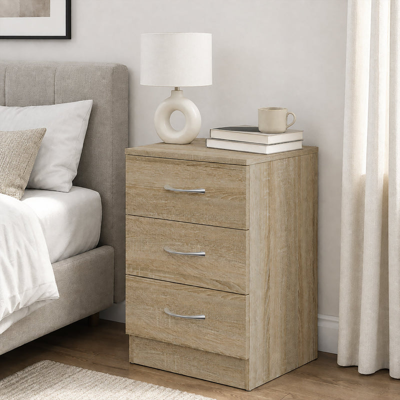 Oak bedside table beside a bed with a lamp, books and a mug on top
