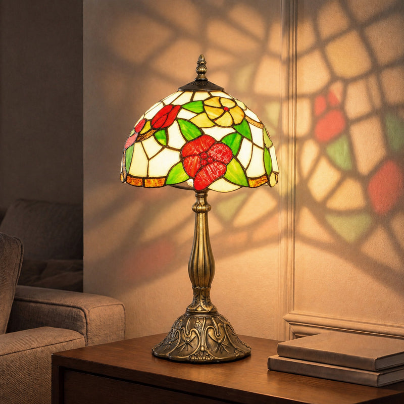 Lit red floral stained glass table lamp on a wooden side table casting a pattern on the wall