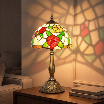 Lit red floral stained glass table lamp on a wooden side table casting a pattern on the wall