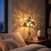 Lit red floral table lamp on a bedside table beside a bed at dusk