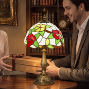 Man unwrapping a gift box with the red floral stained glass table lamp on a desk