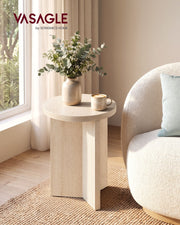 Round travertine beige side table beside a cream sofa with a vase of eucalyptus and a coffee cup