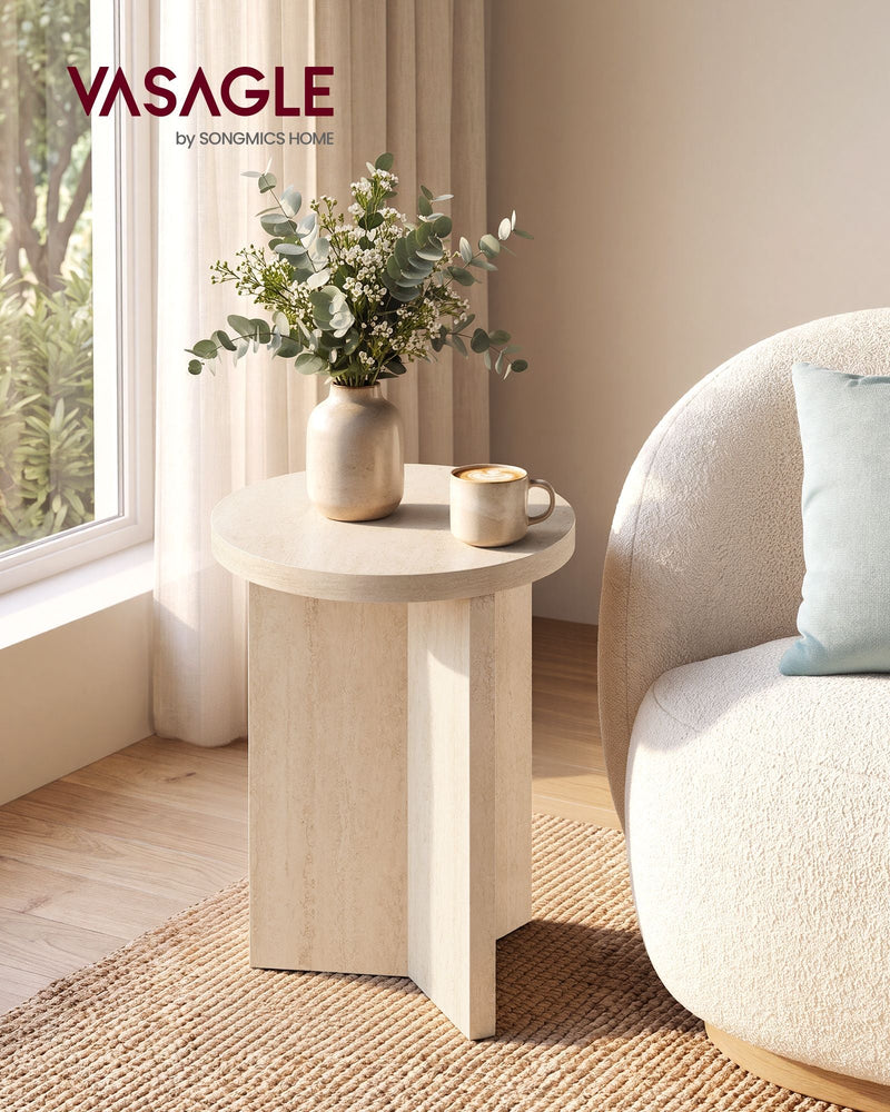 Round travertine beige side table beside a cream sofa with a vase of eucalyptus and a coffee cup