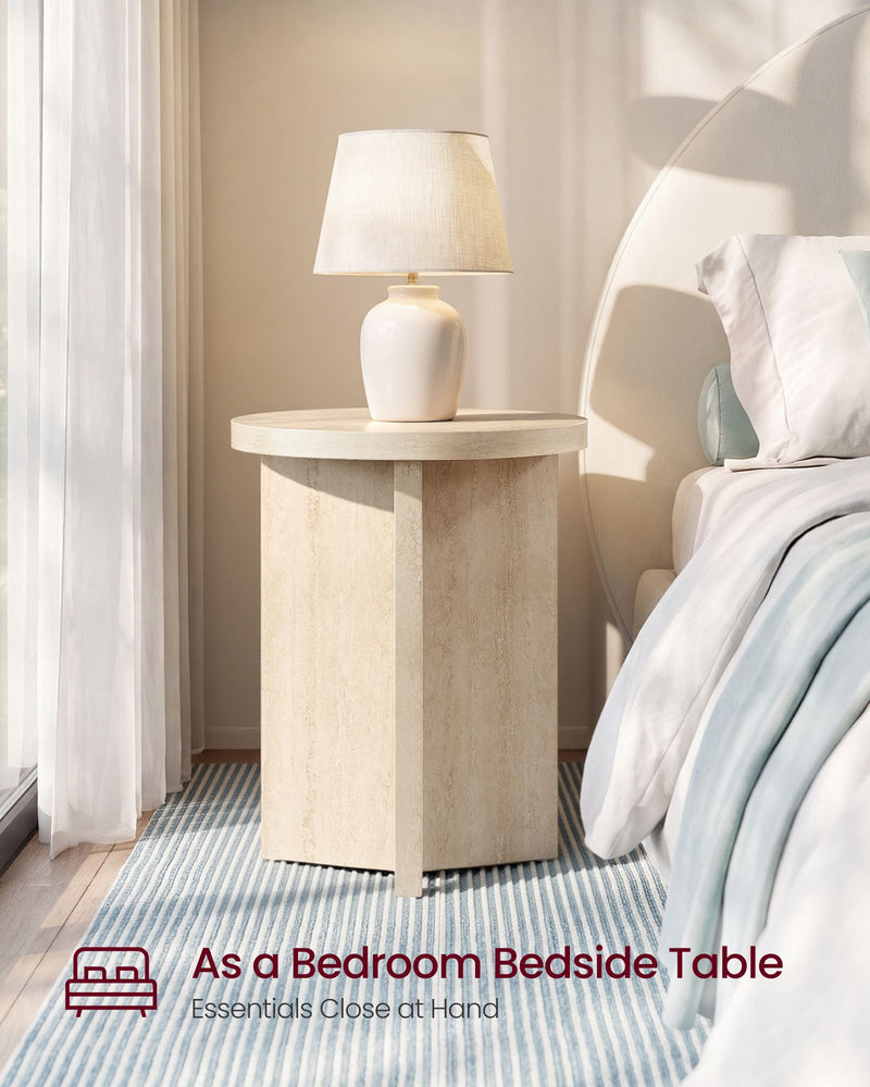 Round side table used as a bedside table holding a table lamp next to a bed