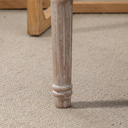 Close-up of a turned wooden bench leg with a distressed finish on carpet