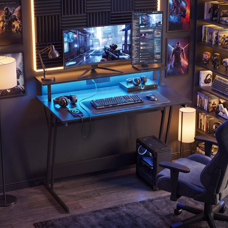 Two tier gaming desk in a dark gaming room with dual monitors and a PC tower alongside