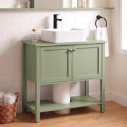 Green under sink cabinet below a vessel sink in a tiled bathroom with a round mirror
